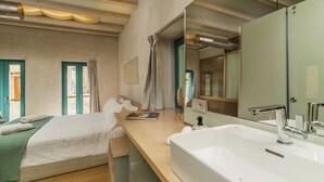 A modern hotel room with a large bed, a wooden desk, a white sink, and a large mirror. - Panaretos Deluxe Maisonette (Chania)