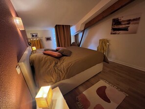 Ett sovrum med en säng, sänglampor, en tavla och ett fönster med gardiner.
