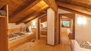 Un dormitorio acogedor en el ático con vigas de madera, una alfombra de piel blanca y una cama con ropa de cama estampada.