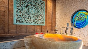 A stone bathtub with a decorative wall panel and a stained glass window. - Experience the Harmony of Luxury, Nature and Wellness! (bali)