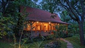 A wooden house with a red roof, surrounded by lush greenery and a stone pathway leading to the entrance. - Experience the Harmony of Luxury, Nature and Wellness! (bali)