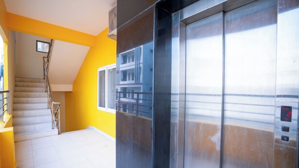 A modern elevator with a digital display, a staircase with metal railings, and a yellow wall. - Yellow Bells Signature (Hyderabad)