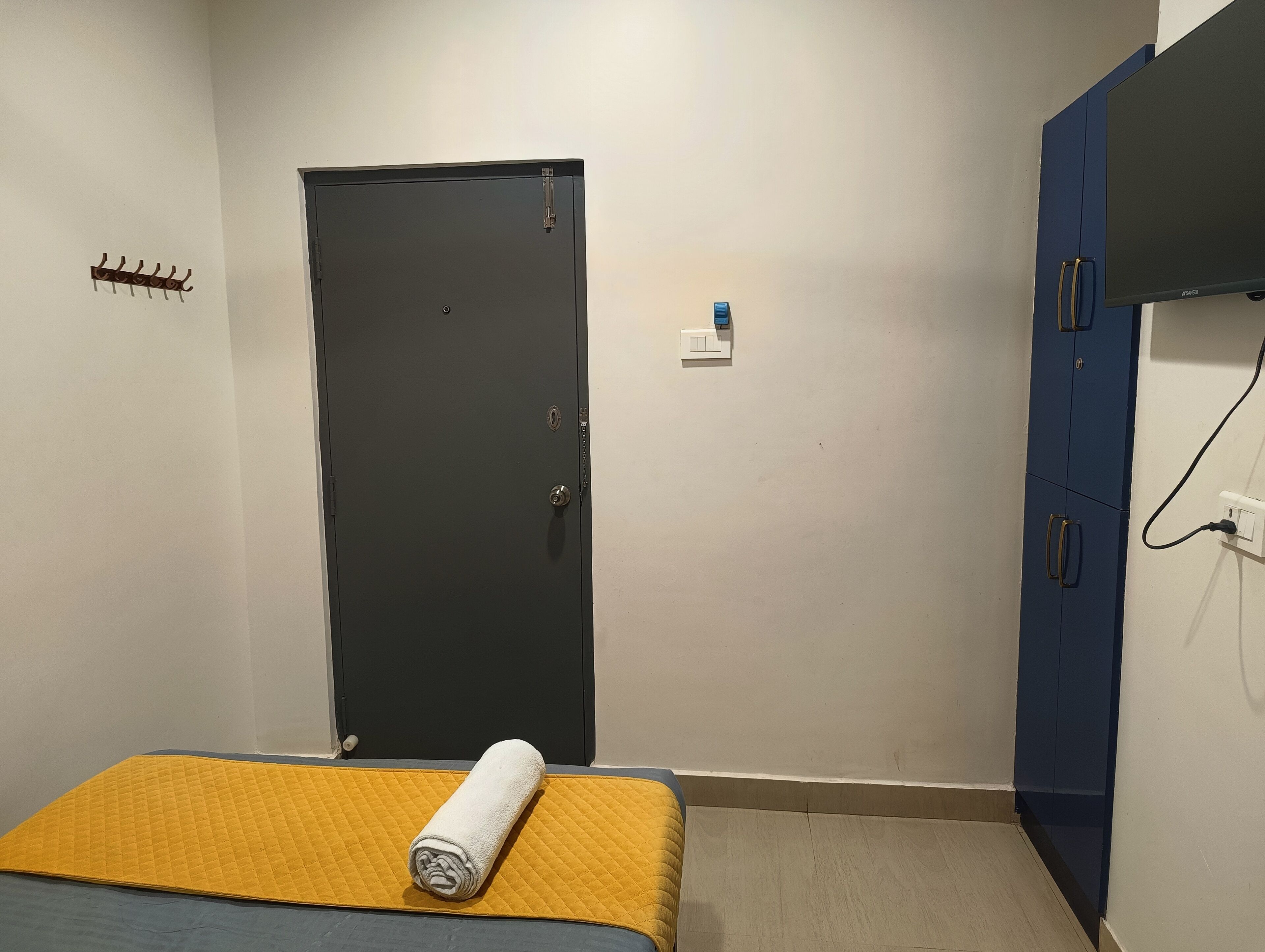 A small room with a bed, a door, a coat rack, and a wardrobe.