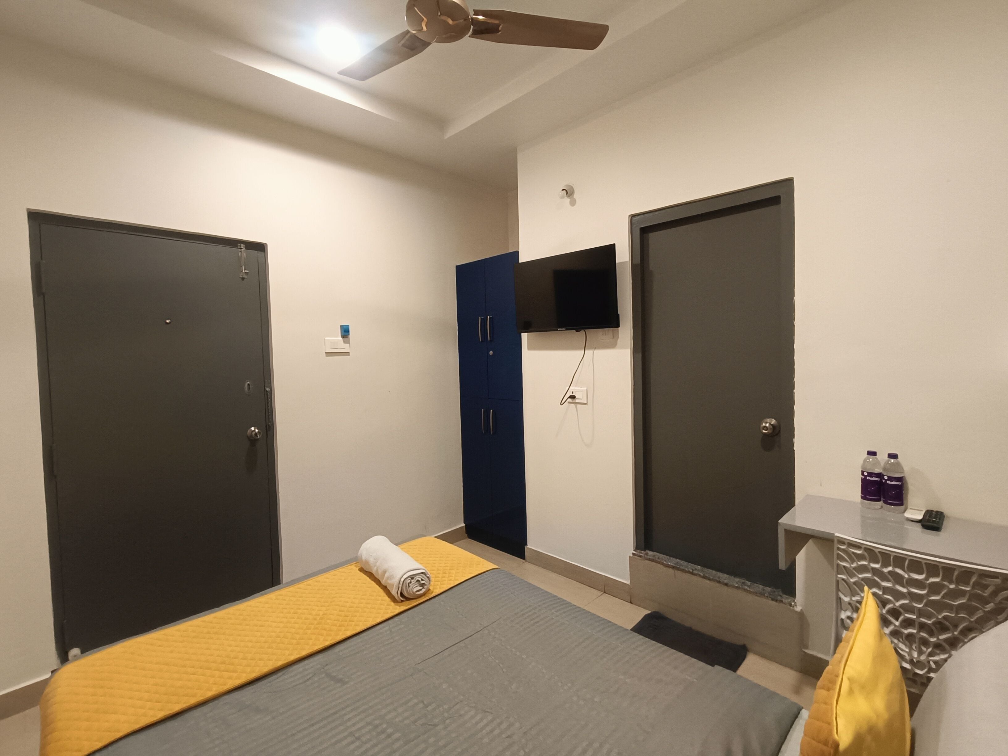 A hotel room with a bed, a desk, a television, and two doors.