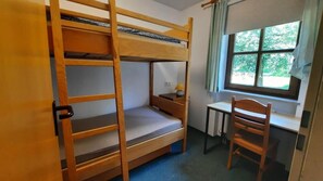 Une chambre avec un lit superposé, un bureau et une chaise, une fenêtre donnant sur un espace verdoyant et une porte.