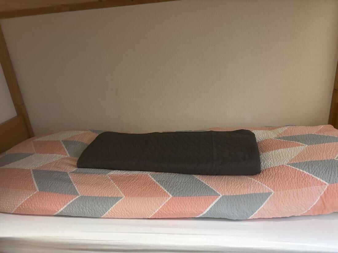 A bed with a geometric patterned pillow and a dark blanket.