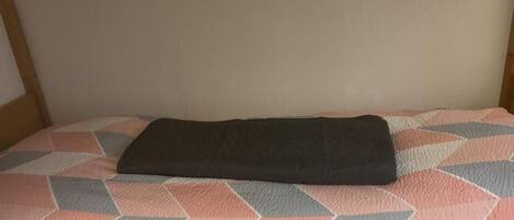 A bed with a geometric patterned pillow and a dark blanket.