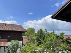 Un bâtiment traditionnel en bois, doté d’un toit en tuiles, entouré d’une végétation luxuriante et surplombé d’un ciel bleu clair.