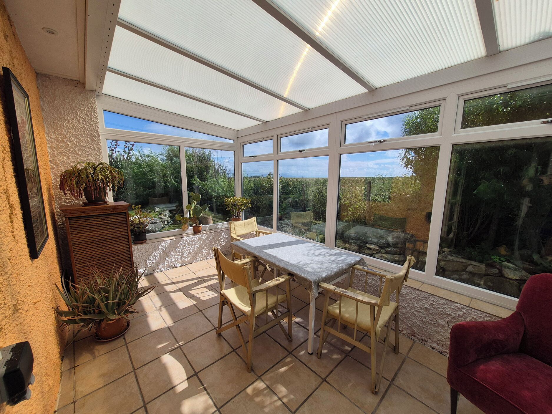 A conservatory with a table and chairs, surrounded by large windows offering a view of the garden.