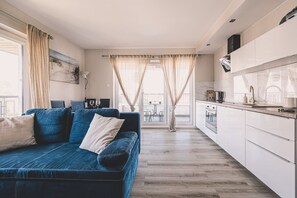 Ett modernt vardagsrum med en blå soffa, en matplats med bord och stolar samt ett kök med vita skåp.
