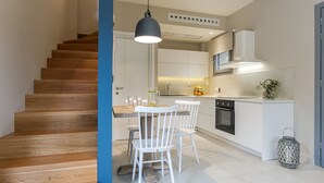 A modern kitchen with white cabinetry, a wooden staircase, and a dining area with white chairs. - Cozy villa in Parga. Pet friendly! (Parga)