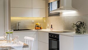 A modern kitchen with white cabinetry, a built-in oven, and a dining area with a table and chairs. - Cozy villa in Parga. Pet friendly! (Parga)