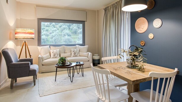 A modern living room with a sofa, a dining table, and a large window. - Cozy villa in Parga. Pet friendly! (Parga)