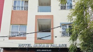 A hotel named "Hotel Jainam Palace" with a modern facade, two visible cars parked in front, and a staircase leading to the entrance. - Hotel Jainam Palace (Ujjain)