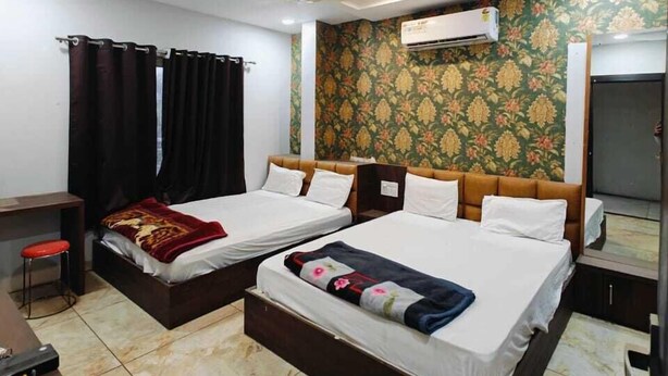 A hotel room with two beds, a desk, a chair, an air conditioning unit, and a ceiling fan. - Hotel Jainam Palace (Ujjain)