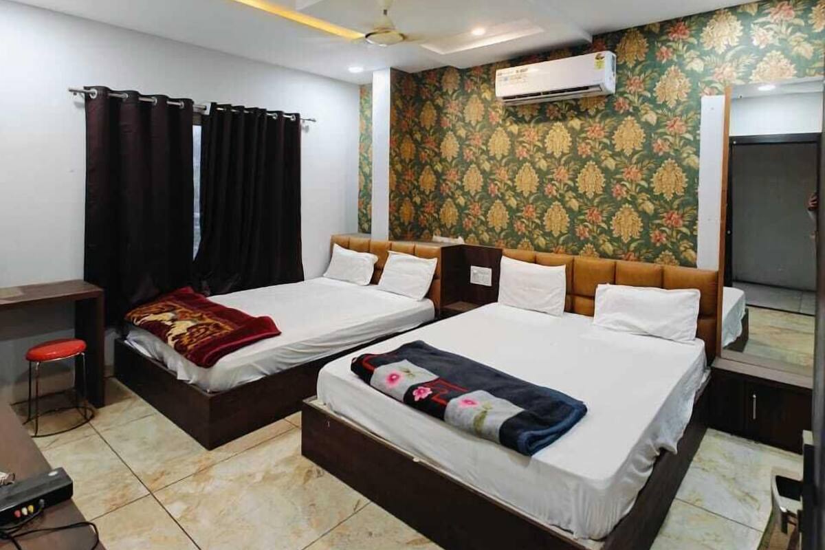 A hotel room with two beds, a desk, a chair, an air conditioning unit, and a ceiling fan.