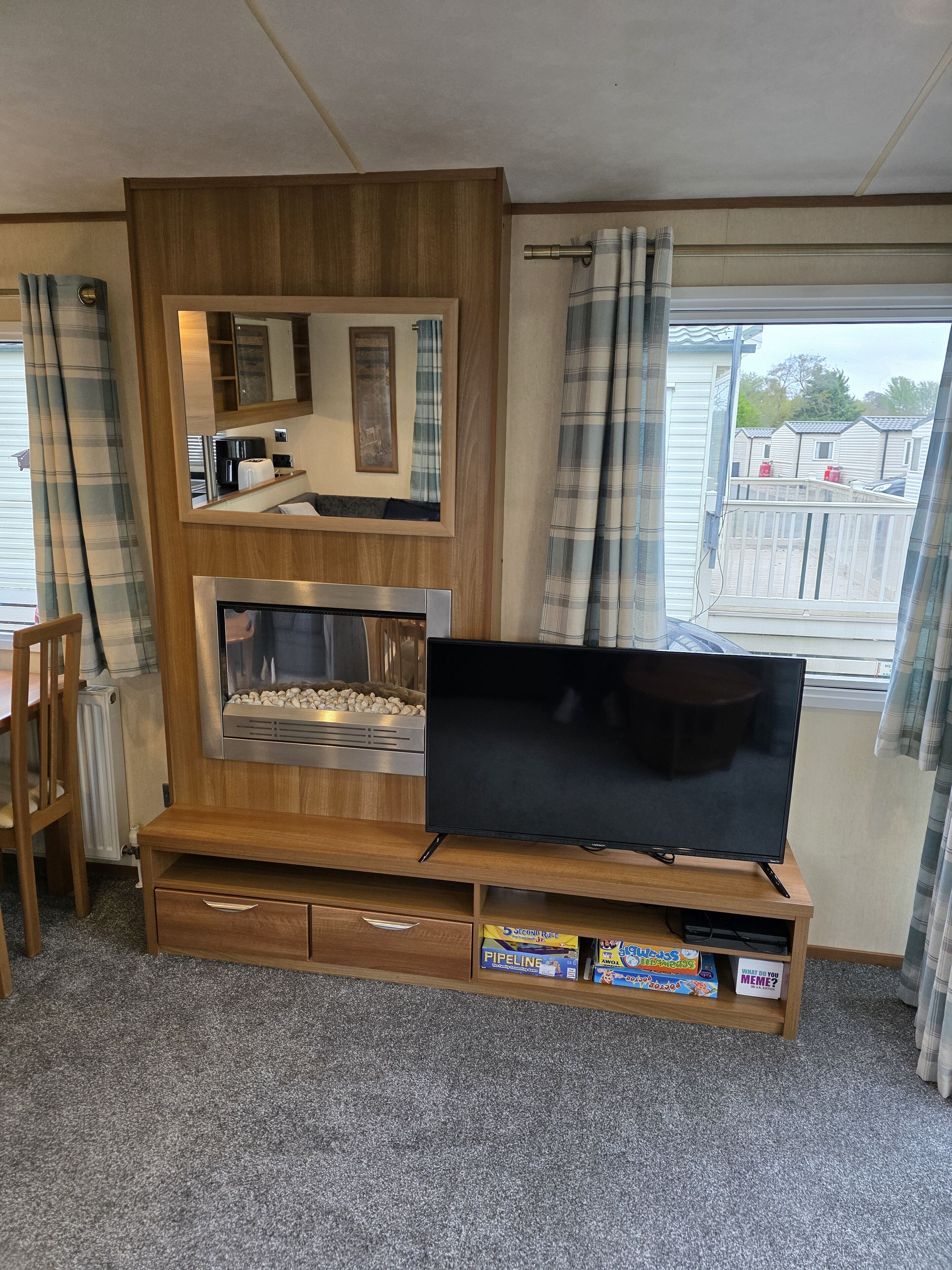 A compact living space with a wooden entertainment unit, a flat-screen TV, a built-in fireplace, and a view of the outside.