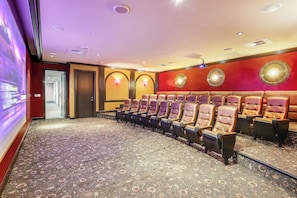 Uma sala de teatro com fileiras de assentos, piso coberto por carpete e parede vermelha com iluminação decorativa.
