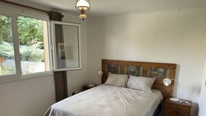 Un dormitorio con cama, mesitas de noche, ventana y lámpara en el techo.