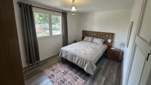 Un dormitorio con cama, mesita de noche, lámpara, ventana con cortinas y alfombra.