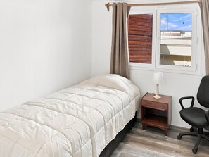 A single bed with a headboard, a bedside table with a lamp, a chair, and a window with curtains. - Oceana Suites Casa Ñuñoa (Santiago)