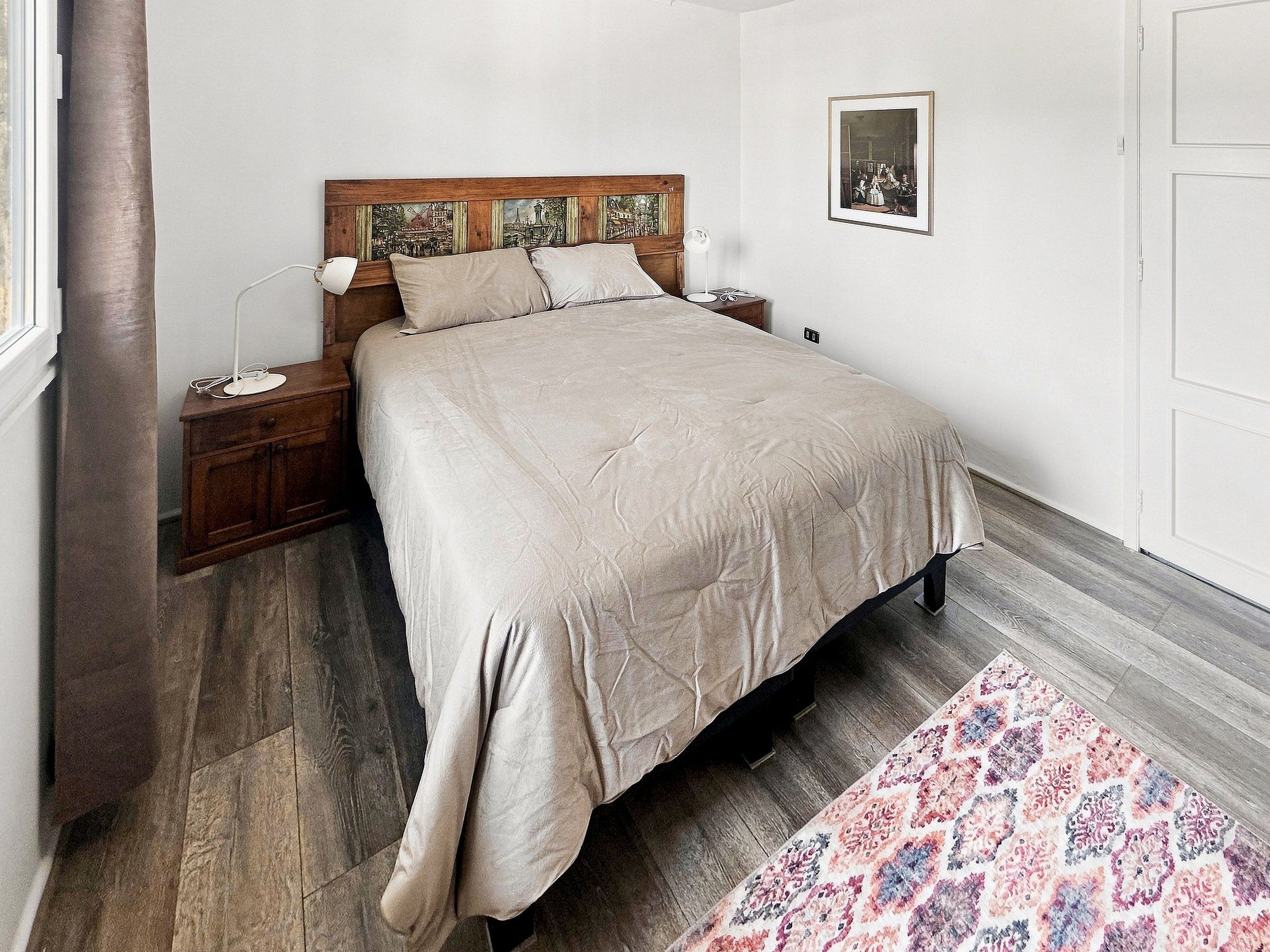 A bedroom with a bed, nightstands, a lamp, a rug, and a framed picture on the wall.