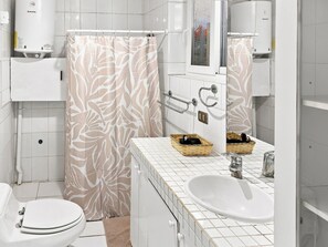 Een moderne badkamer met toilet, wastafel, douche met gordijn met bladmotief en een handdoekrek.