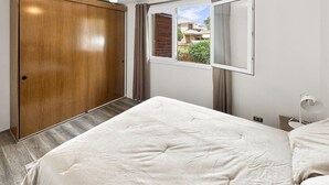 A bedroom with a bed, a wooden wardrobe, a window with curtains, and a view of the outside. - Oceana Suites Casa Ñuñoa (Santiago)
