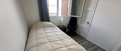 A small, narrow room with a bed, a chair, and a door.