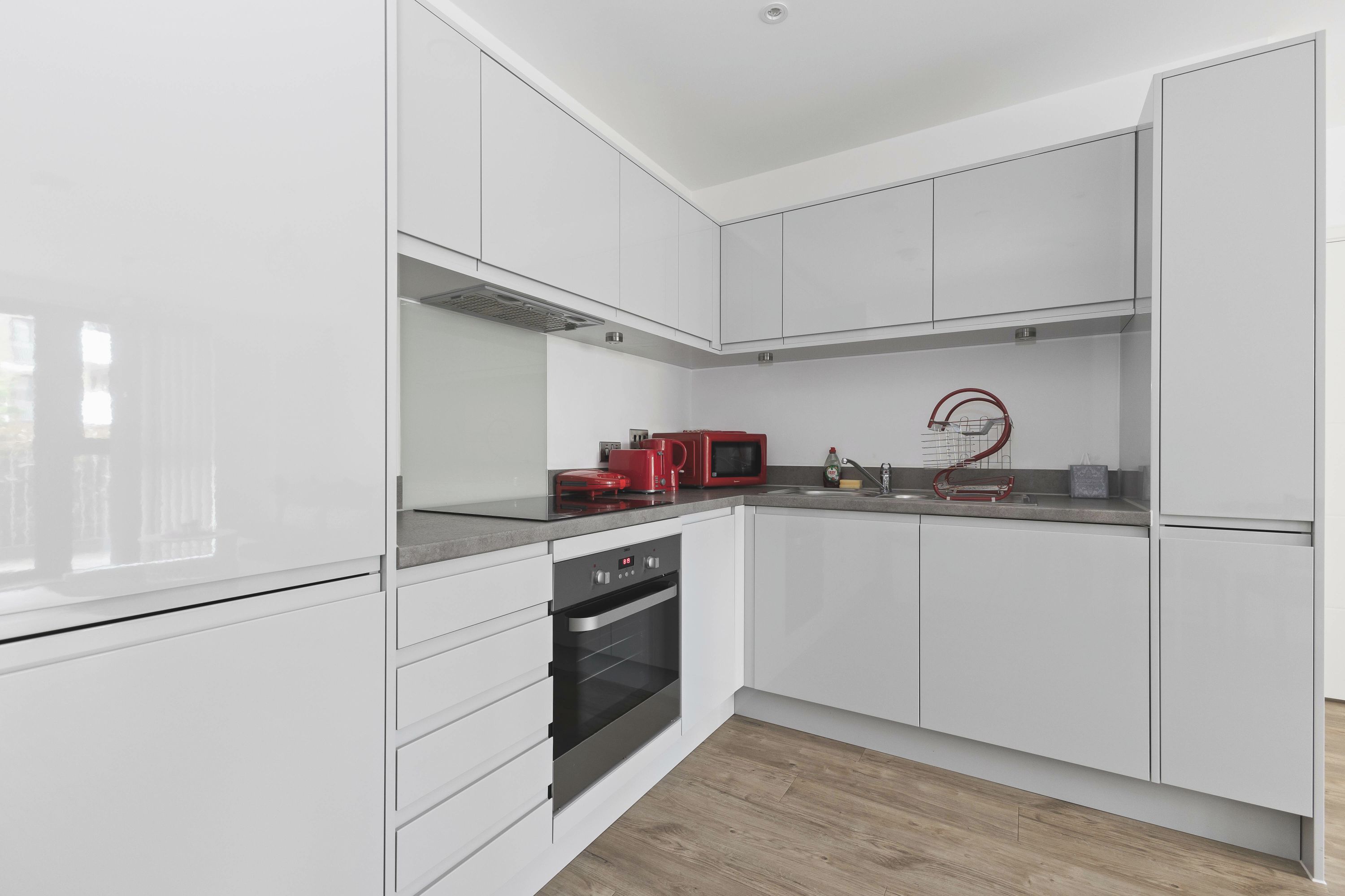 A modern kitchen with white cabinetry, a built-in oven, and a red microwave.