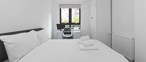 Une chambre avec un grand lit, un bureau avec une chaise, une fenêtre et un radiateur.