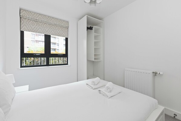 Un dormitorio con cama, ventana con persianas, radiador y armario empotrado.