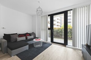 A modern living room with a grey sofa, a round coffee table, and a large sliding glass door leading to an outdoor balcony. - Modern 2 Bed 2 Bath with Patio | Close to Wembley (Greater London)
