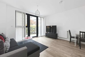 A modern living room with a sofa, a TV, a dining table, and a sliding glass door leading to a balcony. - Modern 2 Bed 2 Bath with Patio | Close to Wembley (Greater London)