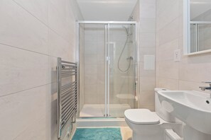 Un baño moderno con ducha envuelta en vidrio, inodoro blanco y lavamanos.