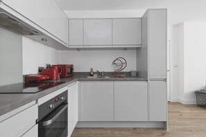 A modern kitchen with white cabinetry, a red induction cooktop, a built-in oven, and a stainless steel sink. - Modern 2 Bed 2 Bath with Patio | Close to Wembley (Greater London)
