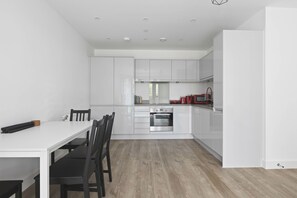 A modern kitchen with white cabinetry, a built-in oven, and a dining area with a white table and chairs. - Modern 2 Bed 2 Bath with Patio | Close to Wembley (Greater London)