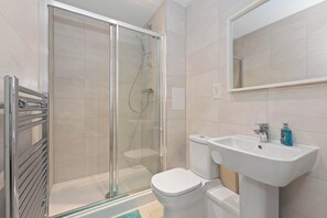 A modern bathroom with a glass-enclosed shower, a white toilet, and a sink with a mirror above it.