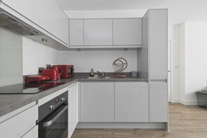 Una cocina moderna con armarios blancos, una cocina de inducción roja y un horno empotrado.