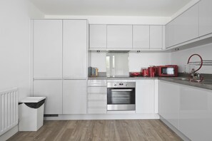 A modern kitchen with white cabinetry, a stainless steel oven, and a red kettle.