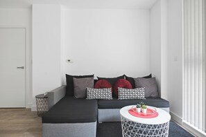 A modern living room with a grey sofa, black and red cushions, a white round coffee table with a red tray, and a geometric white side table.