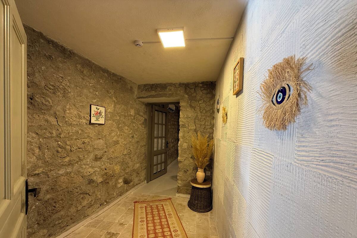 Un passadís amb parets de pedra, una porta, una catifa amb dibuixos i un penjoll decoratiu.