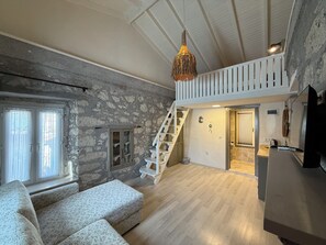 A spacious loft with a high ceiling, exposed stone walls, a staircase, and a cozy seating area.