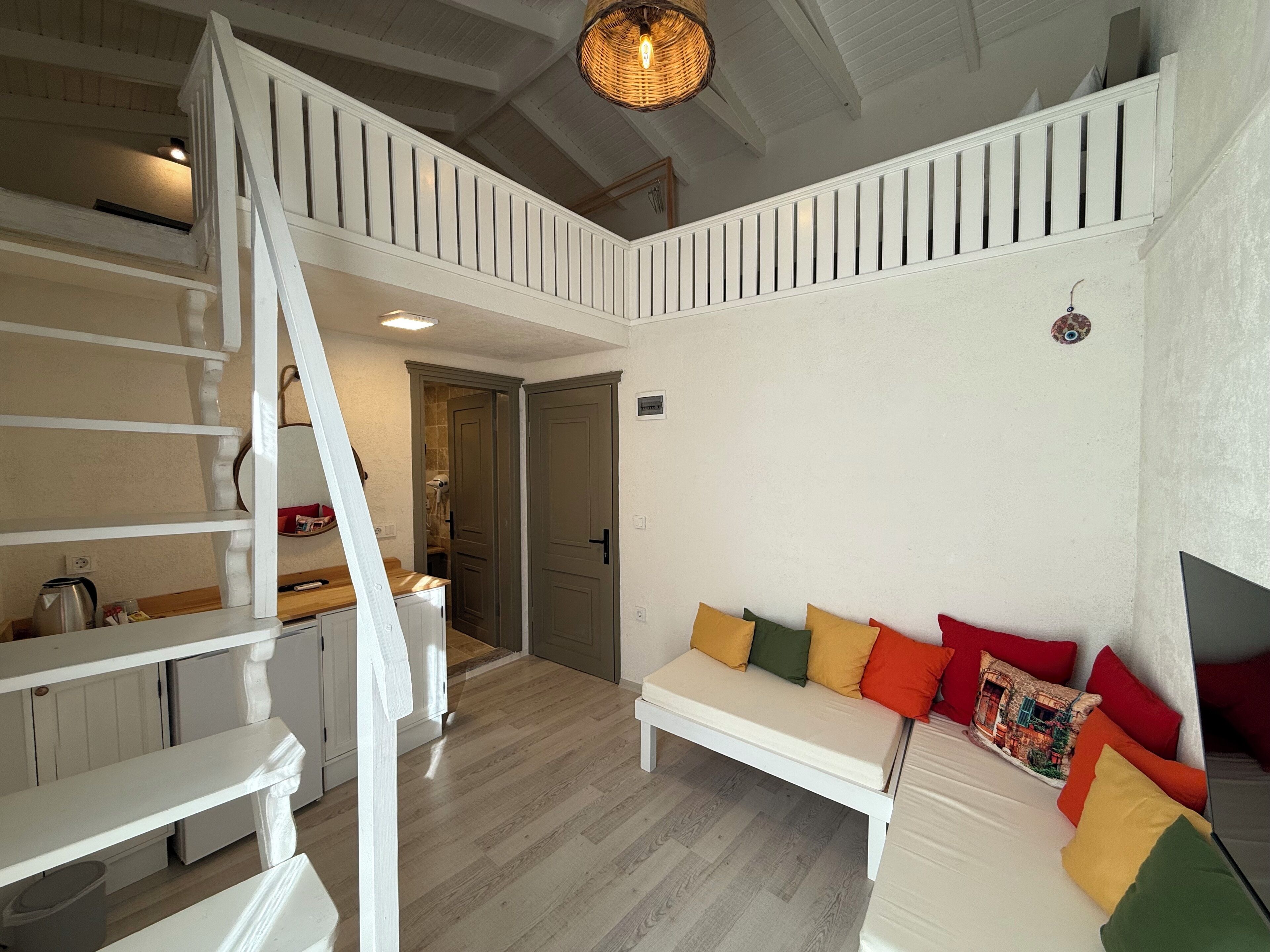 Ein großzügiger Wohnbereich mit einer weißen Wendeltreppe, einem weißen Sofa mit bunten Kissen und Holzboden.