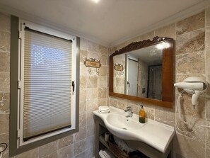 A bathroom with a white sink, a mirror, a hairdryer, and a window with blinds.