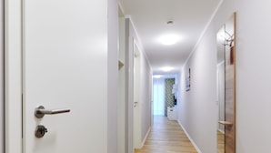 A hallway with wooden flooring, white walls, and a door with a silver handle. - ADAPT APARTMENT HOTEL Wetzlar (Wetzlar)