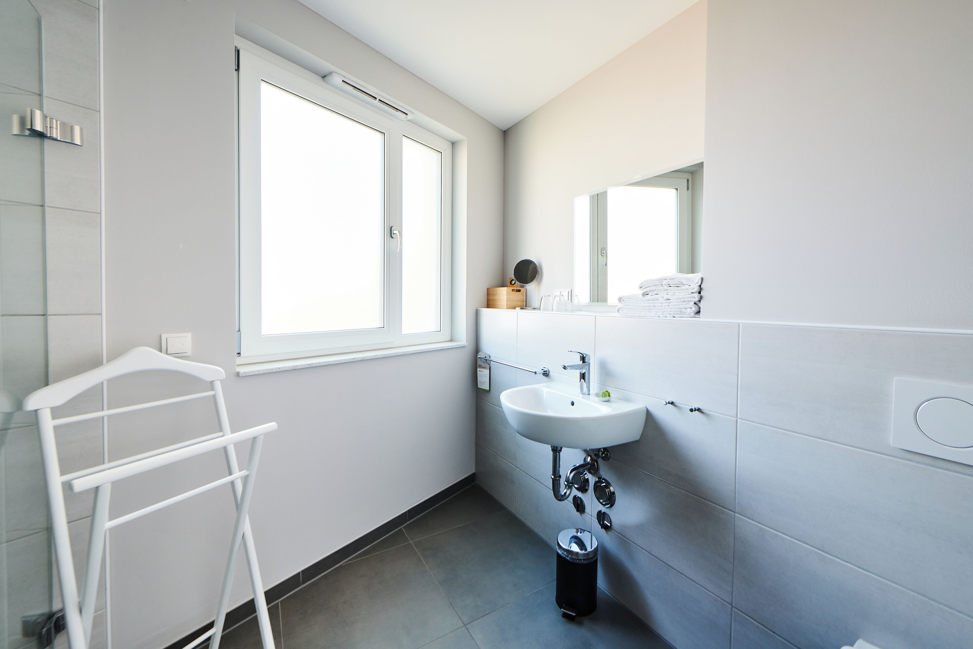 Une salle de bain moderne avec un lavabo blanc, un miroir et un porte-serviettes.