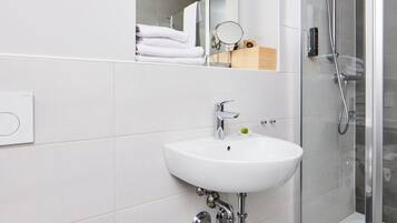A modern bathroom with a white sink, a glass shower enclosure, and a mirror above the sink.