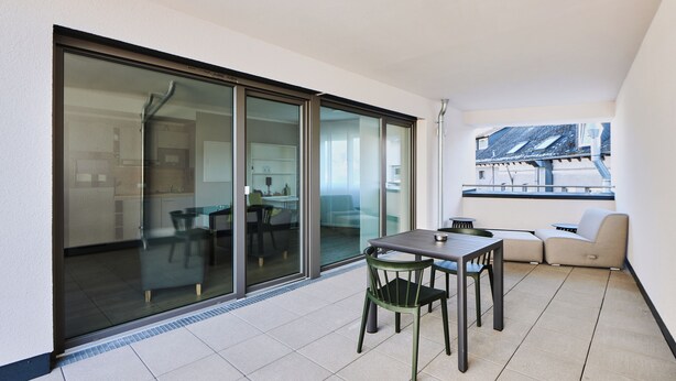 A balcony with a table and chairs, a sofa, and a sliding glass door leading to a kitchen area. - ADAPT APARTMENT HOTEL Wetzlar (Wetzlar)