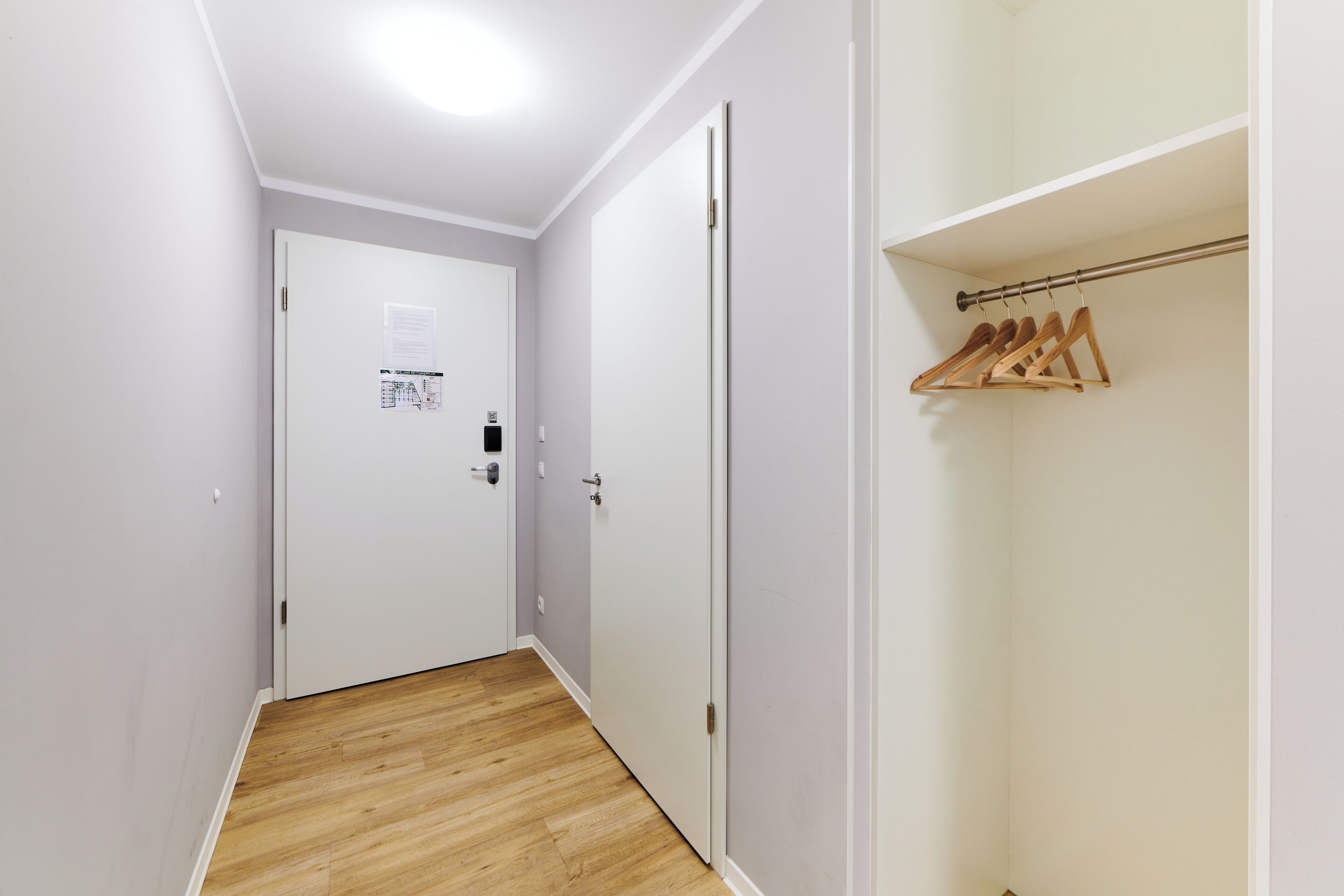 Ein schmaler Flur mit Holzboden, weißen Wänden und einem Schrank mit Holzaufhängern.